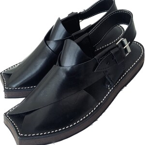 K&ouml;nnte beinhalten: Schwarze Ledersandalen mit Schnallenriemen und einem gen&auml;hten Rand. Die Sandalen haben eine spitze Zehenpartie und eine flache Sohle.