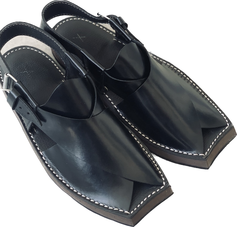 K&ouml;nnte beinhalten: Ein Paar schwarze Ledersandalen mit spitzer Zehenpartie und einem Riemen &uuml;ber dem Fu&szlig;r&uuml;cken. Die Sandalen haben einen wei&szlig;en N&auml;hdetail an den R&auml;ndern.