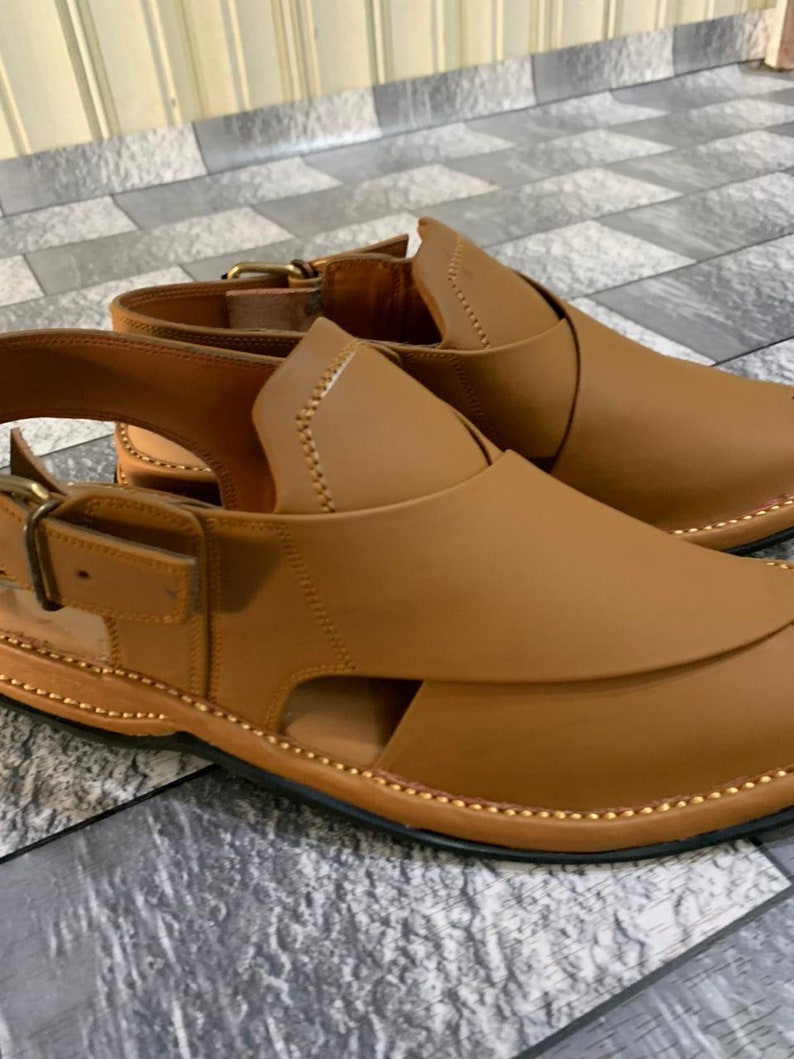 May include: A pair of brown leather sandals with a buckle strap and a decorative stitching detail around the edge.
