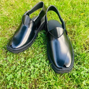 May include: A pair of black leather sandals with a criss-cross strap design. The sandals have a closed toe and a thick sole.