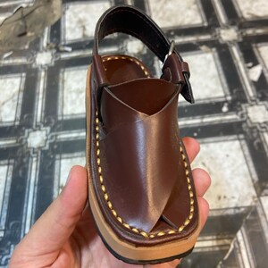 K&ouml;nnte beinhalten: Braune Ledersandalen mit goldenen N&auml;hten und einer Schnalle.