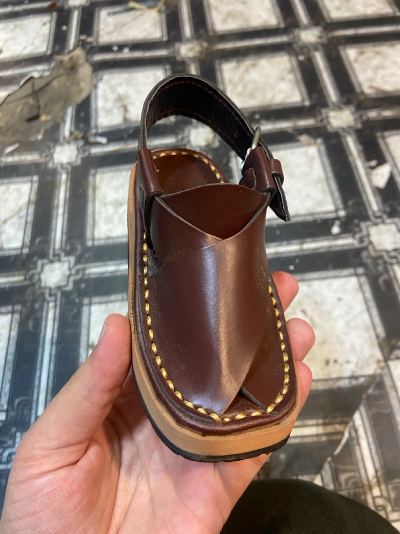 K&ouml;nnte beinhalten: Braune Ledersandalen mit goldenen N&auml;hten und einer Schnalle.