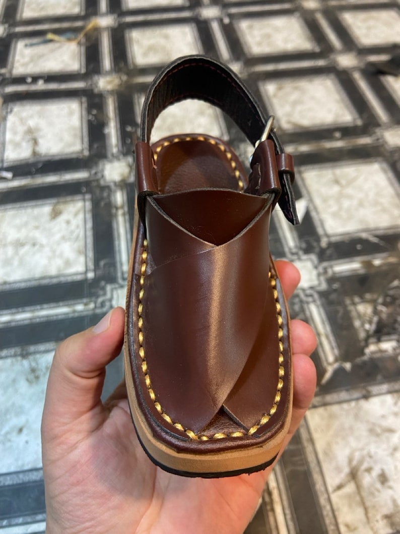 K&ouml;nnte beinhalten: Braune Ledersandalen mit Schnallenverschluss und gelben N&auml;hten.