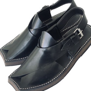 K&ouml;nnte beinhalten: Ein Paar schwarze Ledersandalen mit einer Schnalle. Die Sandalen haben eine spitze Zehenpartie und eine dicke Sohle.