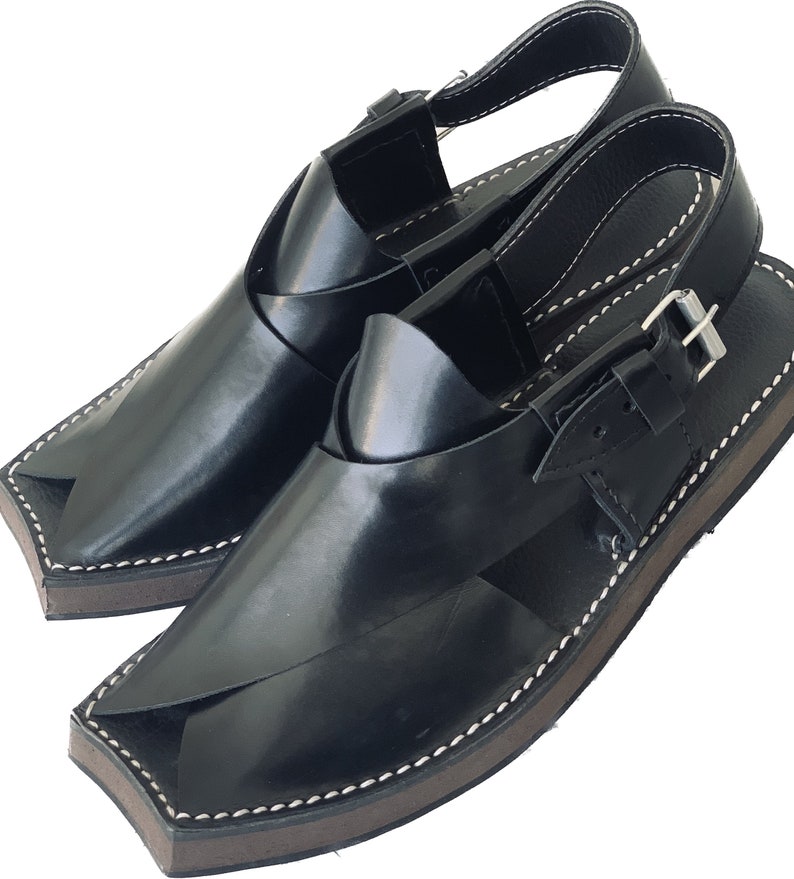 K&ouml;nnte beinhalten: Ein Paar schwarze Ledersandalen mit einer Schnalle. Die Sandalen haben eine spitze Zehenpartie und eine dicke Sohle.
