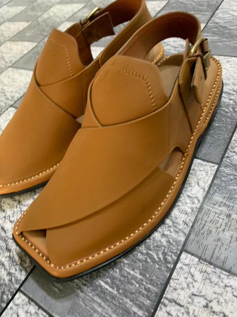 May include: A pair of brown leather sandals with a buckle closure. The sandals have a pointed toe and a stitched design around the edge.