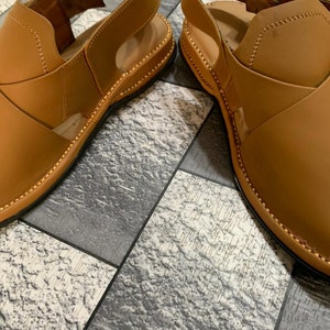 May include: A pair of brown leather sandals with a buckle closure. The sandals have a stitched edge and a textured sole.