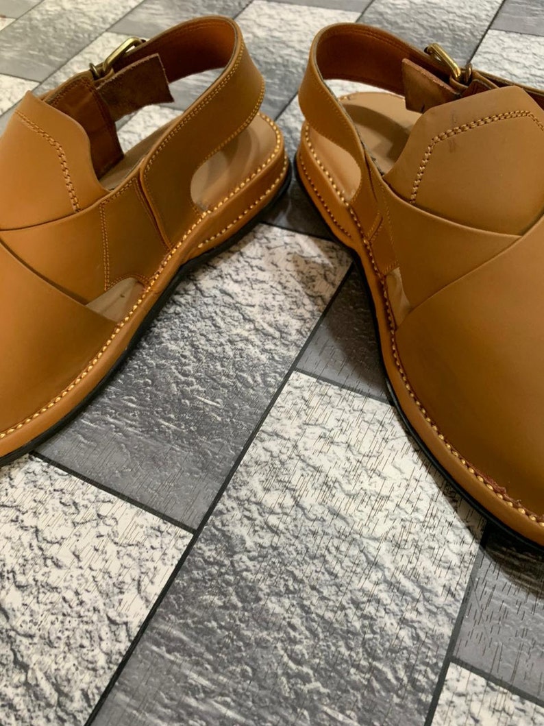 May include: A pair of brown leather sandals with a buckle closure. The sandals have a stitched edge and a textured sole.