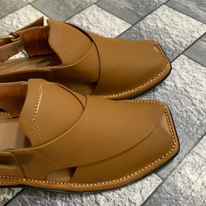 May include: A pair of brown leather sandals with a decorative stitching detail around the edges. The sandals have a closed toe and an open heel.