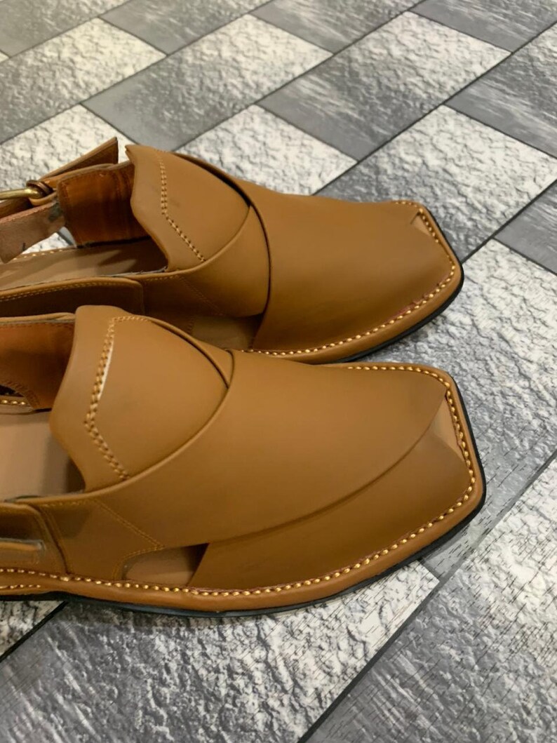 May include: A pair of brown leather sandals with a decorative stitching detail around the edges. The sandals have a closed toe and an open heel.