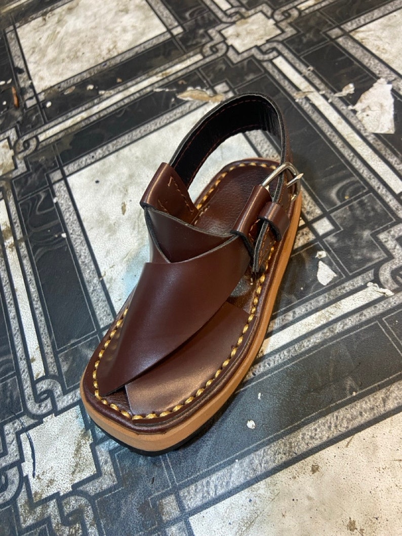 K&ouml;nnte beinhalten: Braune Ledersandalen mit Schnallenverschluss und einem gen&auml;hten Rand. Die Sandalen haben ein schlichtes Design und sind aus hochwertigem Leder gefertigt.