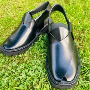 May include: A pair of black leather sandals with a criss-cross strap design. The sandals have a closed toe and a thick, black sole.