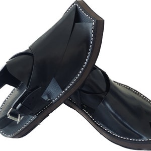 K&ouml;nnte beinhalten: Ein Paar schwarze Ledersandalen mit geschlossener Zehenpartie und offenem Absatz. Die Sandalen haben eine braune Ledersohle und eine wei&szlig;e Naht an der Kante.
