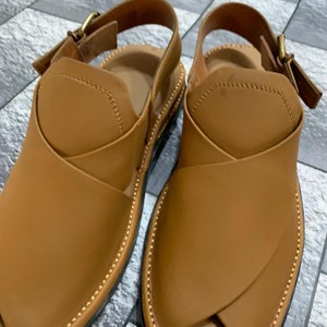 May include: A pair of brown leather sandals with a buckle closure. The sandals have a pointed toe and a decorative stitching detail around the edge.