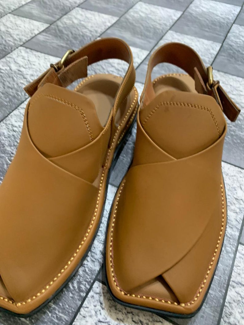 May include: A pair of brown leather sandals with a buckle closure. The sandals have a pointed toe and a decorative stitching detail around the edge.
