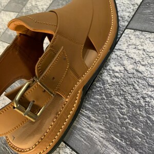 May include: A pair of brown leather sandals with a buckle closure and a stitched edge. The sandals have an open toe design and a thick sole.