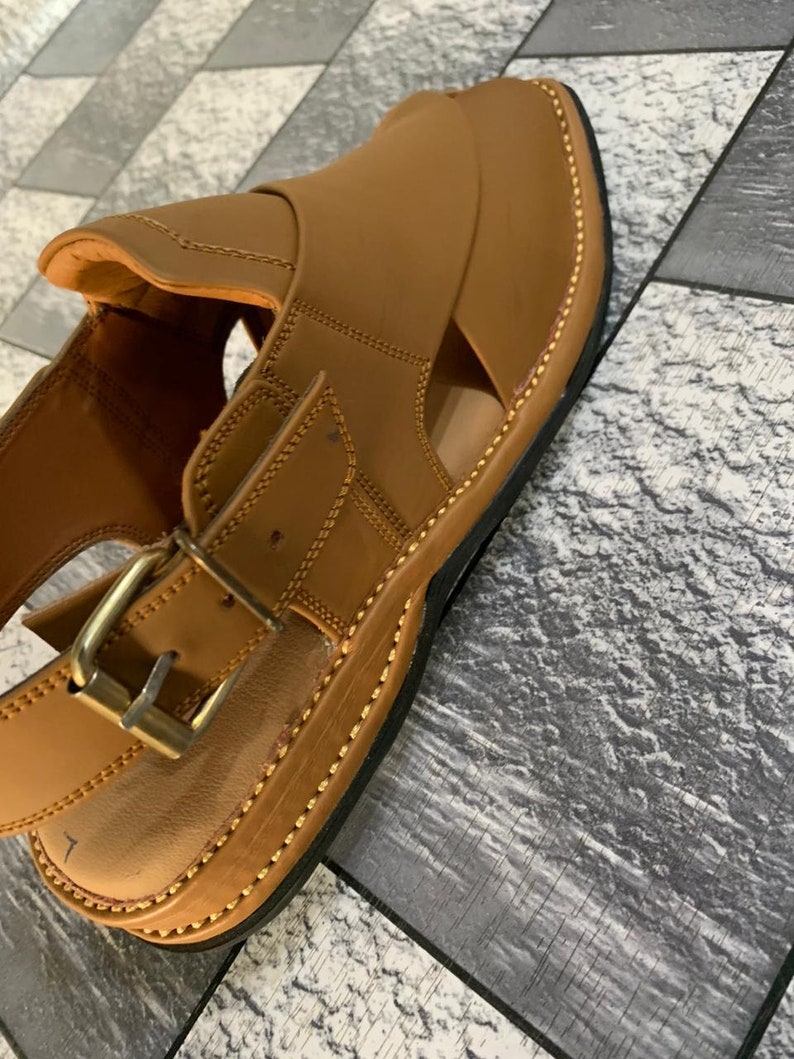 May include: A pair of brown leather sandals with a buckle closure and a stitched edge. The sandals have an open toe design and a thick sole.