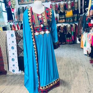 K&ouml;nnte beinhalten: Ein leuchtend t&uuml;rkisfarbenes Kleid mit langen &Auml;rmeln und aufwendiger Stickerei. Das Kleid hat farbenfrohe Blumen- und geometrische Muster um den Halsausschnitt, die Taille und die Manschetten. Das Kleid wird auf einer Schaufensterpuppe pr&auml;sentiert und zeigt traditionelle ethnische Kleidung.