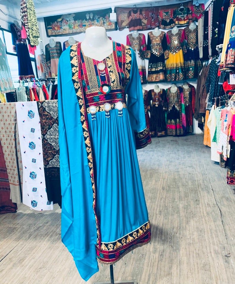 K&ouml;nnte beinhalten: Ein leuchtend t&uuml;rkisfarbenes Kleid mit langen &Auml;rmeln und aufwendiger Stickerei. Das Kleid hat farbenfrohe Blumen- und geometrische Muster um den Halsausschnitt, die Taille und die Manschetten. Das Kleid wird auf einer Schaufensterpuppe pr&auml;sentiert und zeigt traditionelle ethnische Kleidung.