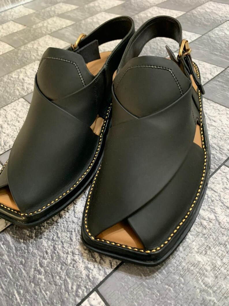 May include: A pair of black leather sandals with a gold buckle and stitching. The sandals have a pointed toe and a strap that goes around the ankle.