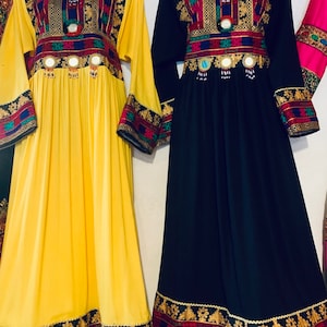 K&ouml;nnte beinhalten: Zwei lang&auml;rmlige Kleider werden pr&auml;sentiert. Eines ist gelb, das andere schwarz. Beide haben eine verzierte Stickerei in Rot, Gold, Blau und Gr&uuml;n um den Halsausschnitt, die Taille und die Manschetten. Die Kleider haben ein flie&szlig;endes, bodenlanges Design mit dekorativen Spiegelakzenten.