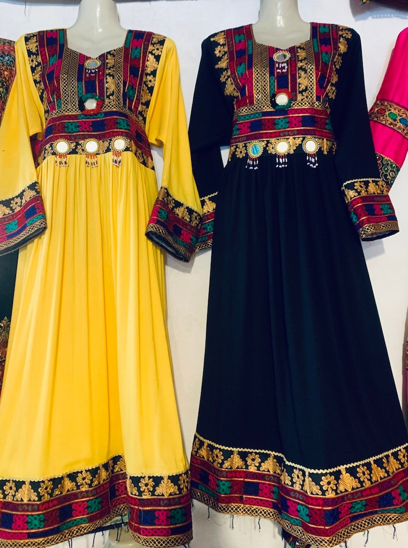 K&ouml;nnte beinhalten: Zwei lang&auml;rmlige Kleider werden pr&auml;sentiert. Eines ist gelb, das andere schwarz. Beide haben eine verzierte Stickerei in Rot, Gold, Blau und Gr&uuml;n um den Halsausschnitt, die Taille und die Manschetten. Die Kleider haben ein flie&szlig;endes, bodenlanges Design mit dekorativen Spiegelakzenten.