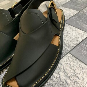 May include: Black leather sandals with a gold buckle and stitching. The sandals have a closed toe and an open heel.