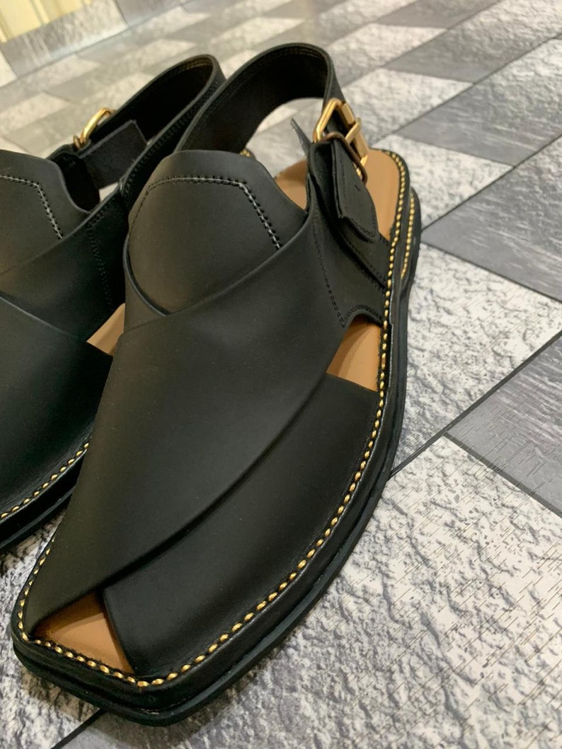 May include: Black leather sandals with a gold buckle and stitching. The sandals have a closed toe and an open heel.