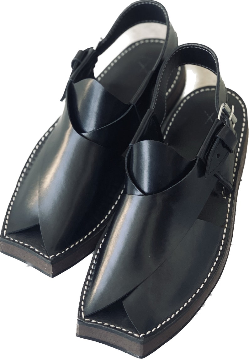 K&ouml;nnte beinhalten: Ein Paar schwarze Ledersandalen mit spitzer Zehenpartie und Schnallenverschluss. Die Sandalen haben ein wei&szlig;es N&auml;hdetail an den R&auml;ndern.