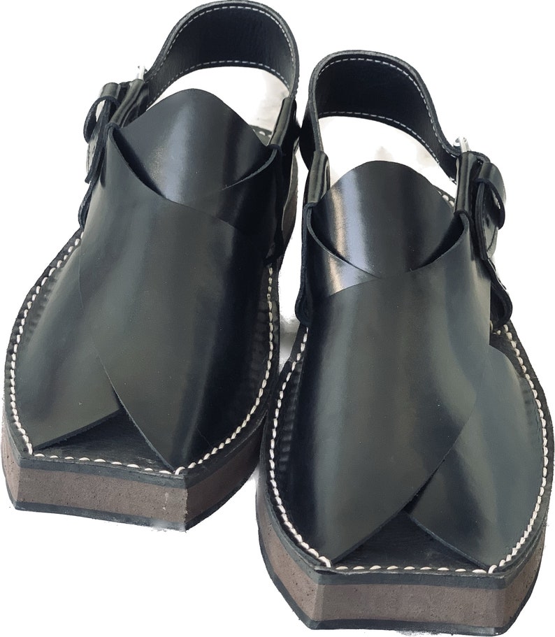 K&ouml;nnte beinhalten: Ein Paar schwarze Ledersandalen mit einem Kreuzriemen-Design. Die Sandalen haben eine braune Sohle und wei&szlig;e N&auml;hte.