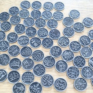 K&ouml;nnte beinhalten: Eine Sammlung von 72 silberfarbenen Metallmarken mit komplizierten schwarzen Designs. Jede Marke zeigt ein einzigartiges Symbol oder Sigil.