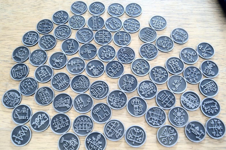 K&ouml;nnte beinhalten: Eine Sammlung von 72 silberfarbenen Metallmarken mit komplizierten schwarzen Designs. Jede Marke zeigt ein einzigartiges Symbol oder Sigil.