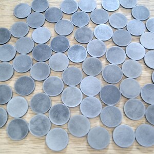 K&ouml;nnte beinhalten: Eine gro&szlig;e Sammlung runder, grauer, metallischer Scheiben. Die Scheiben sind in einem zuf&auml;lligen Muster auf einer Holzoberfl&auml;che angeordnet.