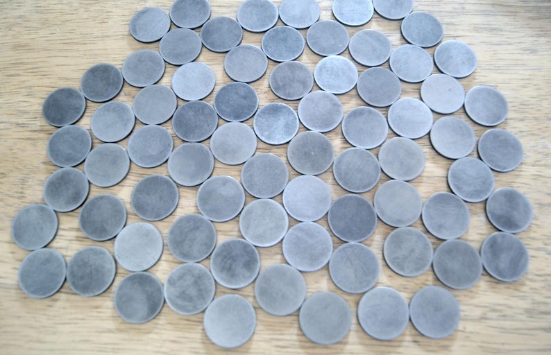 K&ouml;nnte beinhalten: Eine gro&szlig;e Sammlung runder, grauer, metallischer Scheiben. Die Scheiben sind in einem zuf&auml;lligen Muster auf einer Holzoberfl&auml;che angeordnet.