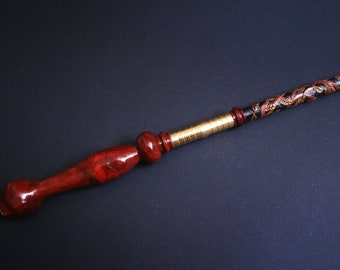 Könnte beinhalten: Ein Zauberstab aus Holz mit einem dunkelbraunen Griff und einem schwarz-goldenen, bemalten Schaft mit einem dekorativen Design. Der Zauberstab ist etwa 33 cm lang.