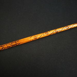 May include: A wooden wand with intricate carvings and designs. The wand is brown and has a light brown finish. The carvings are in a dark brown color.