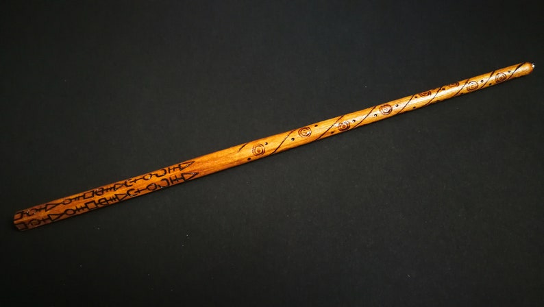 May include: A wooden wand with intricate carvings and designs. The wand is brown and has a light brown finish. The carvings are in a dark brown color.