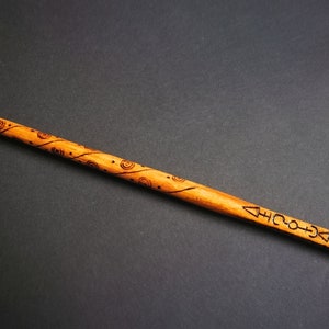 May include: A wooden wand with a brown finish and intricate carvings. The wand is decorated with a swirling pattern and symbols.