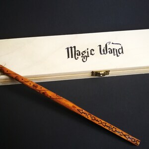 May include: A wooden wand with intricate carvings and a wooden box with the words "Magic Wand" printed on it.
