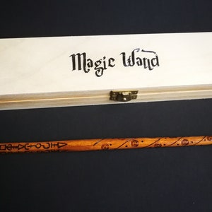 May include: A wooden box with the words "Magic Wand" written on the top. The box is closed and has a brass latch. A wooden wand with intricate carvings is lying next to the box.