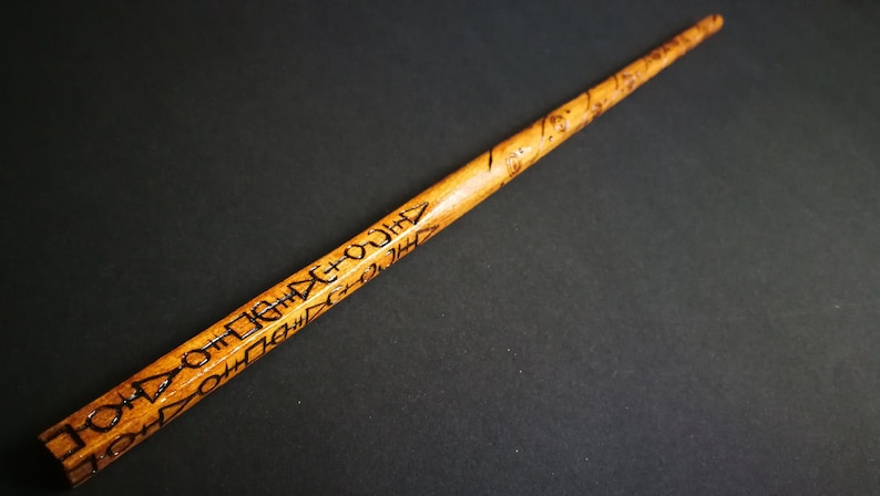 May include: A wooden wand with intricate carvings and a brown finish. The wand is about 12 inches long and has a pointed tip.