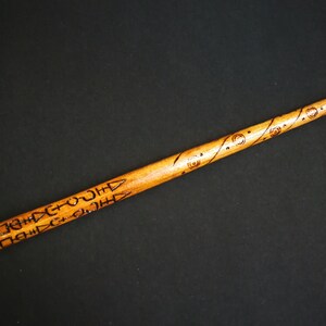 May include: A wooden wand with intricate carvings and a dark brown finish. The wand is approximately 12 inches long.