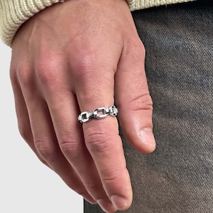 Puede incluir: Un anillo de cadena de plata con eslabones ovalados. El anillo se lleva en el dedo índice de una mano.