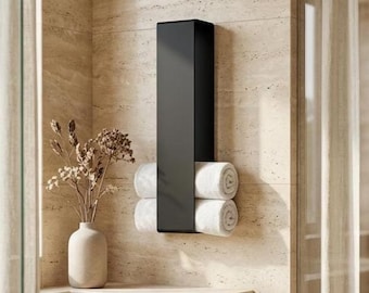 May include: A modern black towel rack mounted on a beige tiled wall. The rack holds four rolled white towels. A vase with dried flowers sits on a nearby countertop, adding a touch of decor to the bathroom.