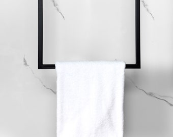 May include: A white towel hanging on a black metal towel rack against a white marble background.