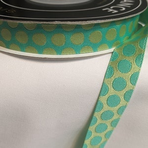 May include: A spool of teal and gold polka dot ribbon. The ribbon is on a white surface.