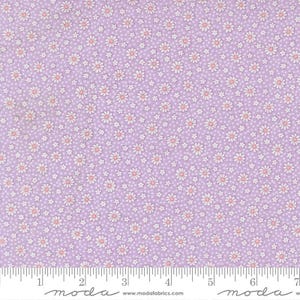 May include: A light purple fabric with a repeating pattern of small white daisies with pink centers and tiny white dots. The fabric is marked with a ruler along the bottom edge.