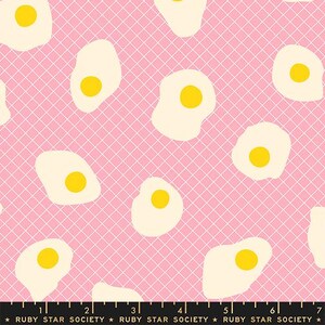 May include: Pink fabric with a repeating pattern of fried eggs. The eggs have yellow yolks and off-white whites. A white grid pattern overlays the eggs. The text "RUBY STAR SOCIETY" is at the bottom.