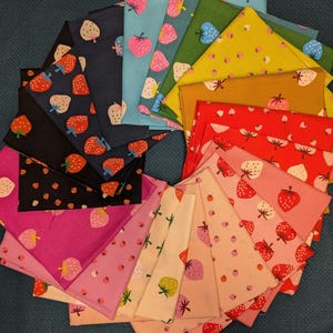 May include: A collection of colorful fabric squares, each featuring a strawberry pattern. The fabrics vary in color, including black, pink, blue, green, and yellow, with red and white strawberries. The squares are arranged in a circular pattern.