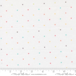 May include: White fabric with a repeating pattern of small, colorful crosses in shades of red, yellow, teal, and gray. The crosses are evenly spaced across the surface. A ruler is at the bottom of the fabric.